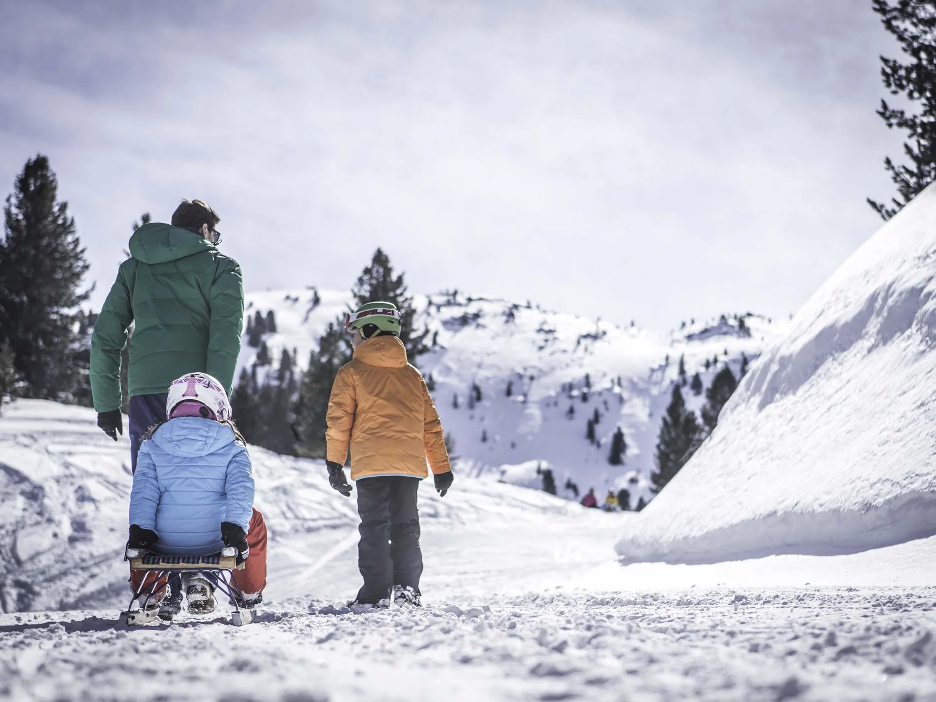 Il Lodenwirt a Vandoies | Hotel, residence e ristorante Famiglia con un bambino su una slitta lungo un sentiero innevato in montagna
