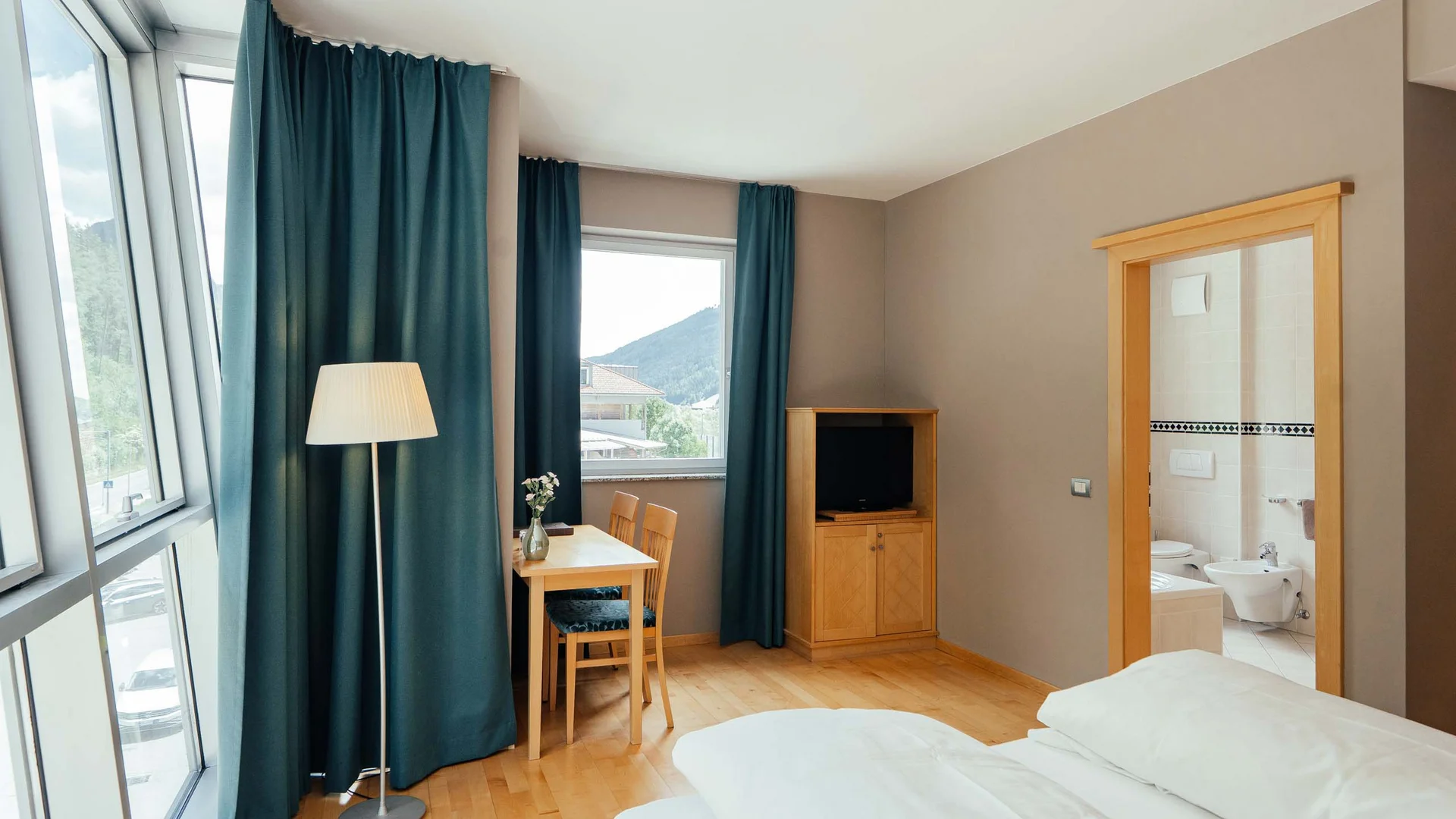 Camera d'hotel luminosa con letto matrimoniale, tavolo, sedie e vista sulle montagne