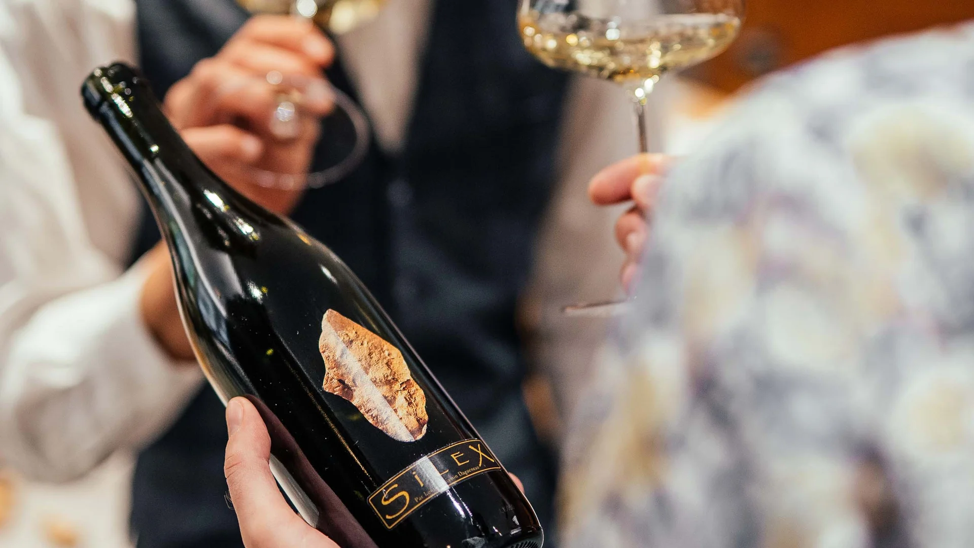 Freut euch auf dieses Hotel in Vintl. Person hält Weinflasche, andere riecht an Weinglas mit Weißwein