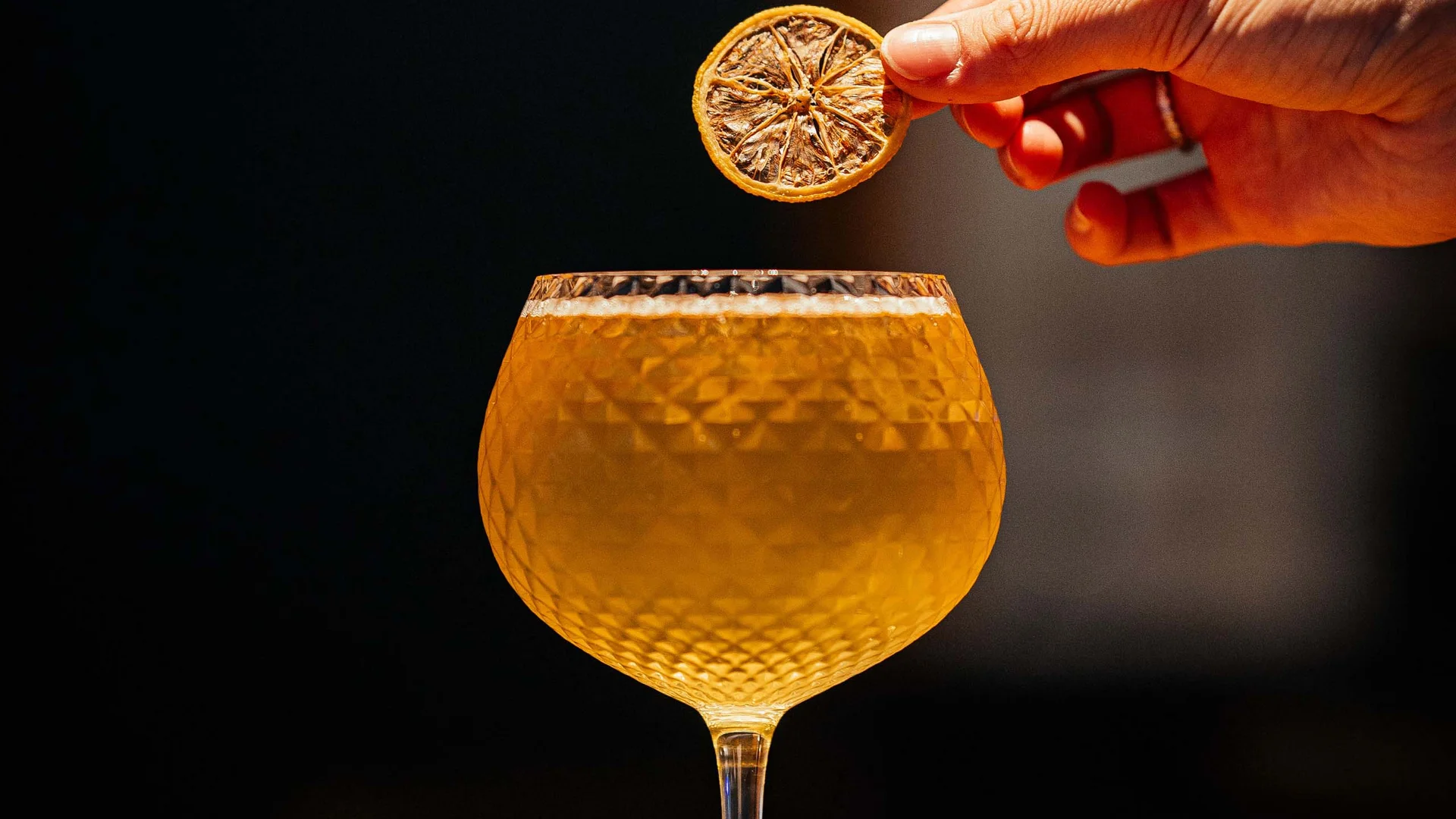 Mano che posa una fetta di limone essiccato su una bevanda in un bicchiere di cristallo