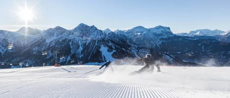 Sciatore su una pista preparata davanti a montagne innevate e seggiovia
