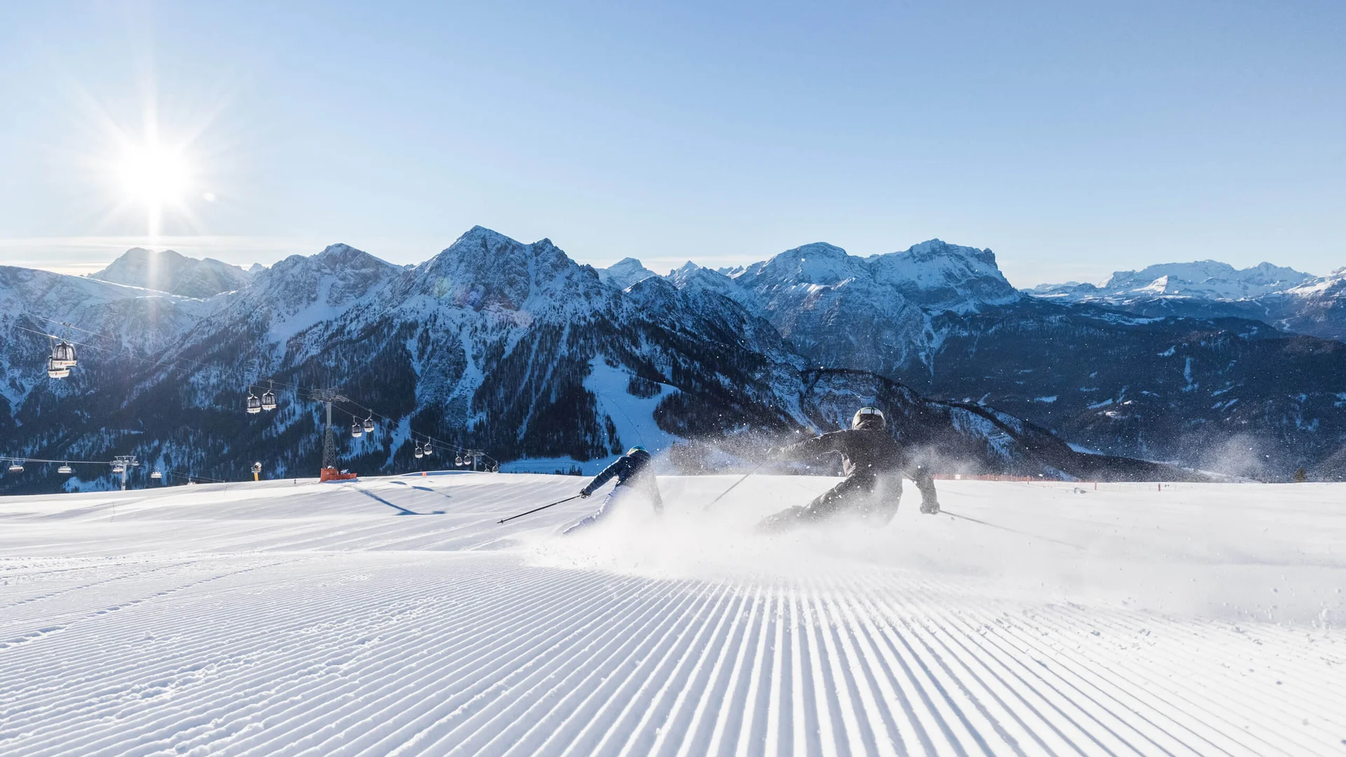 Hotel & Residence Lodenwirt photo gallery Skier on a groomed slope with snowy mountains and a chairlift