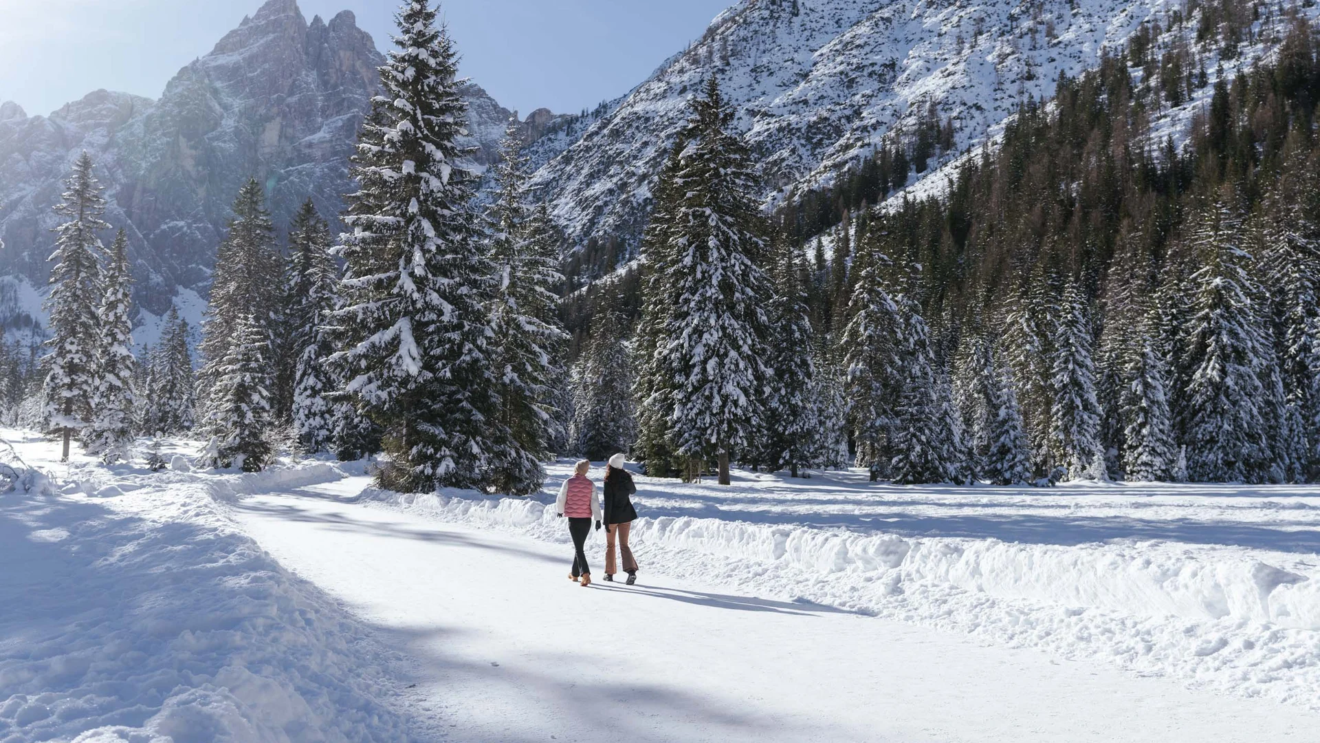 Hotel & Residence Lodenwirt photo gallery Two people walk through a snowy fir forest beneath snow-covered mountains