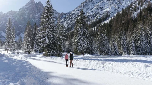 Il Lodenwirt a Vandoies | Hotel, residence e ristorante Due persone camminano in un bosco innevato ai piedi di montagne coperte di neve