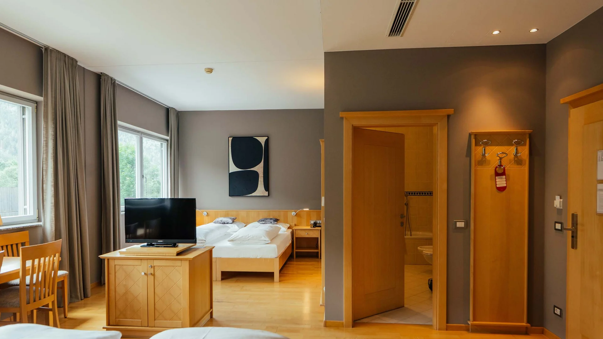 Camera d'hotel luminosa con letto matrimoniale, TV, tavolo da pranzo e bagno aperto