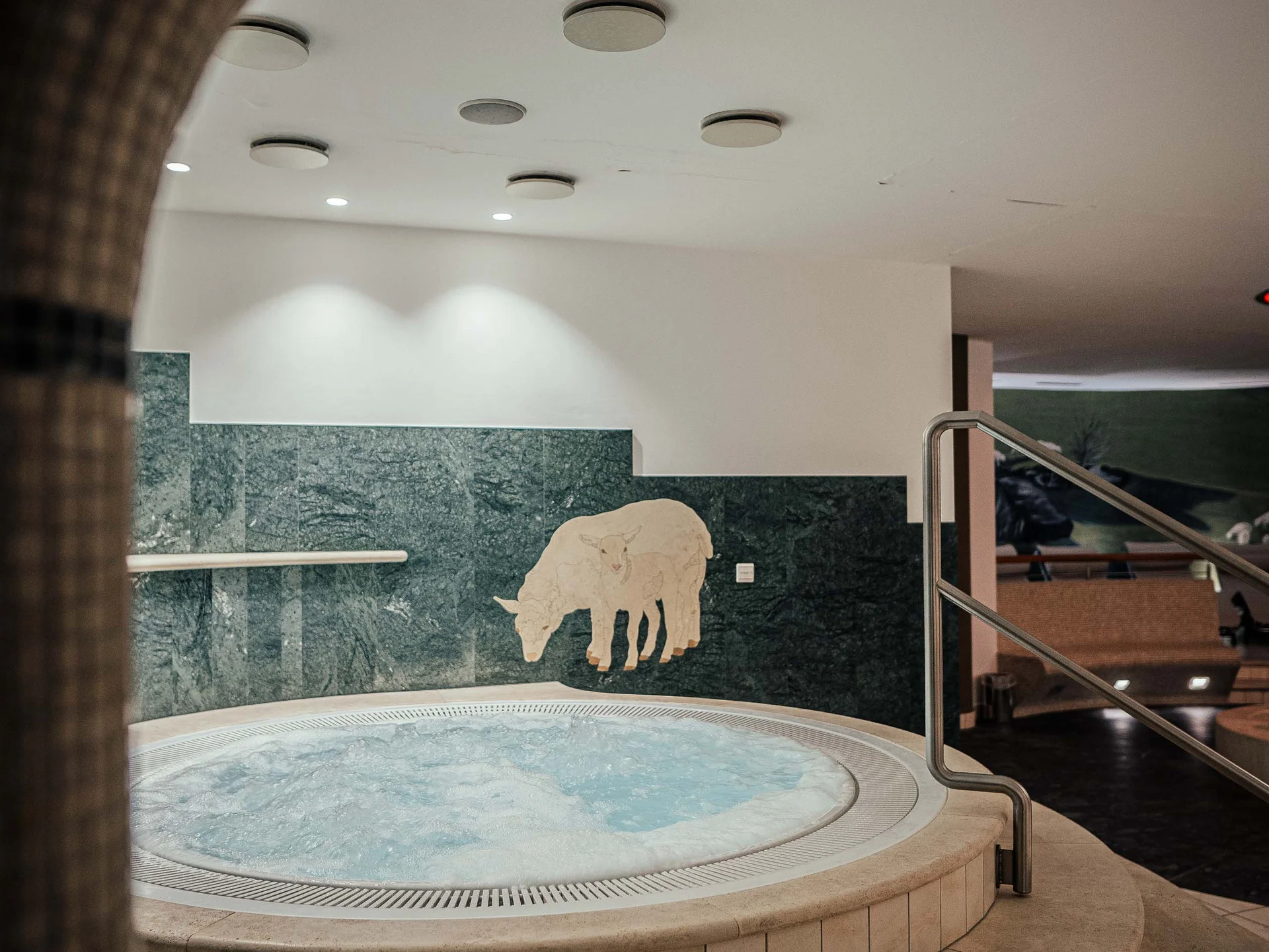 Il vostro hotel con spa vicino a Brunico Runder Whirlpool mit Treppen und Kuhrelief an grüner Wand im Innenbereich