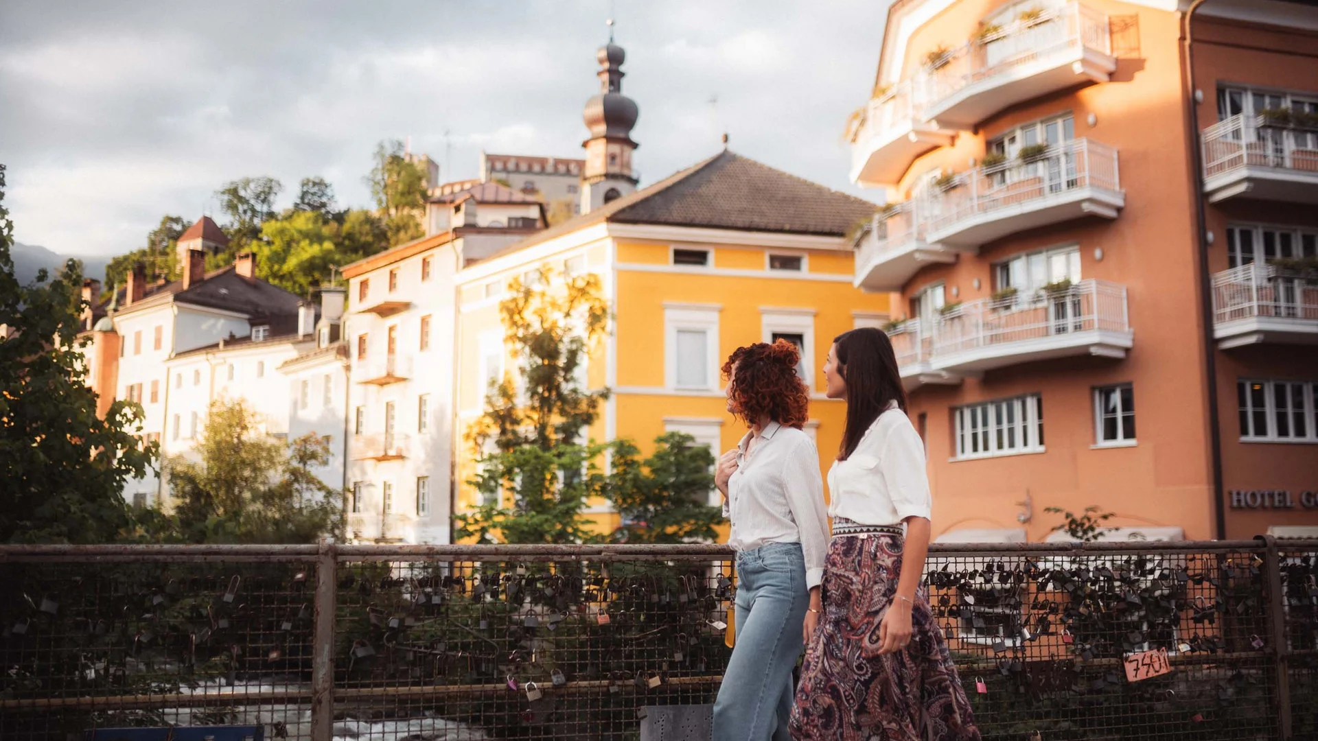 Due donne camminano su un ponte davanti a edifici colorati e a un campanile