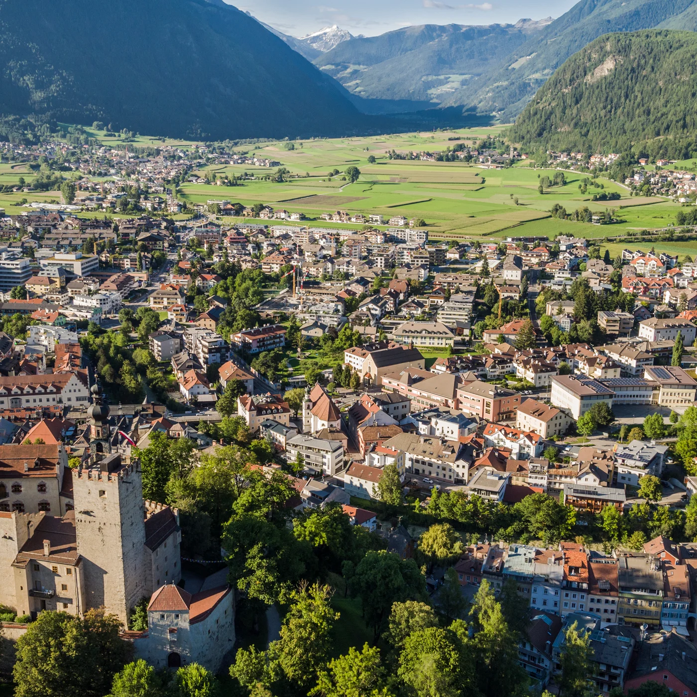Le vostre vacanze in Val Pusteria Veduta aerea di una città con castello e montagne sullo sfondo