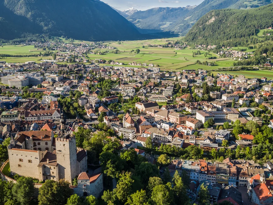 Le vostre vacanze in Val Pusteria Veduta aerea di una città con castello e montagne sullo sfondo