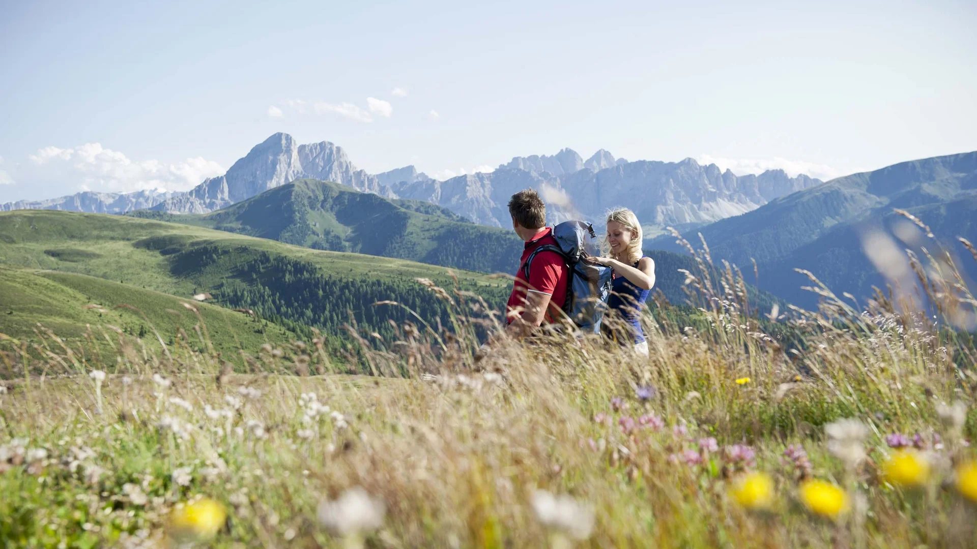 Hotel & Residence Lodenwirt photo gallery Two hikers with backpacks in a flower-filled meadow with alpine mountains in the background