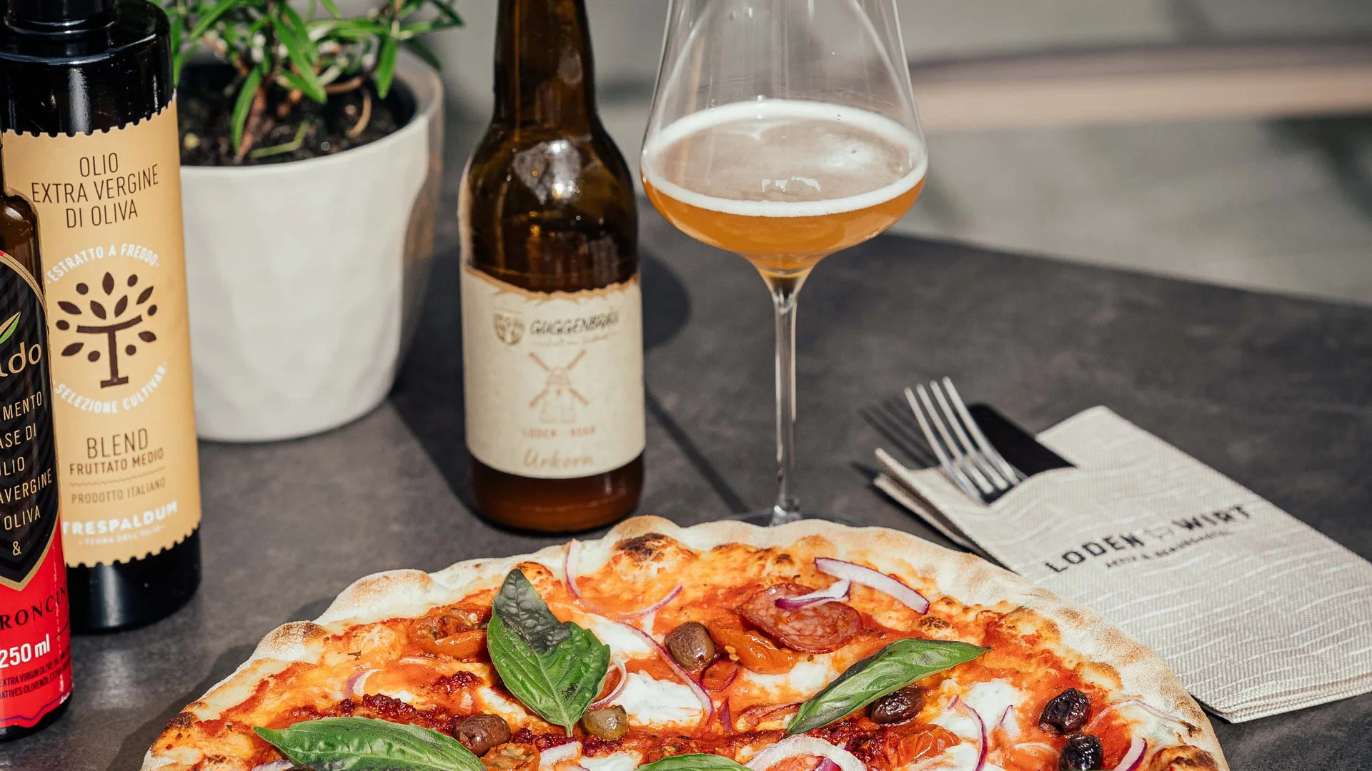 Pizza italiana con basilico, olio d'oliva, bottiglia di birra e bicchiere sul tavolo