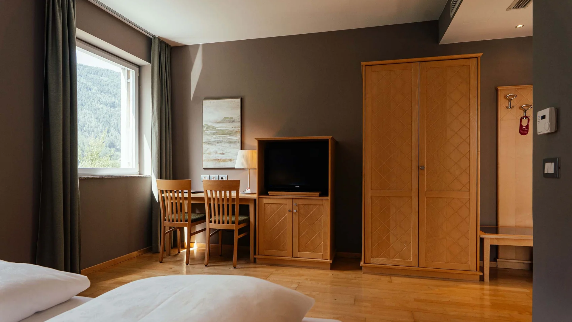 Hotelzimmer mit Holzmöbeln, Fernseher, Schreibtisch und Fenster mit Bergblick