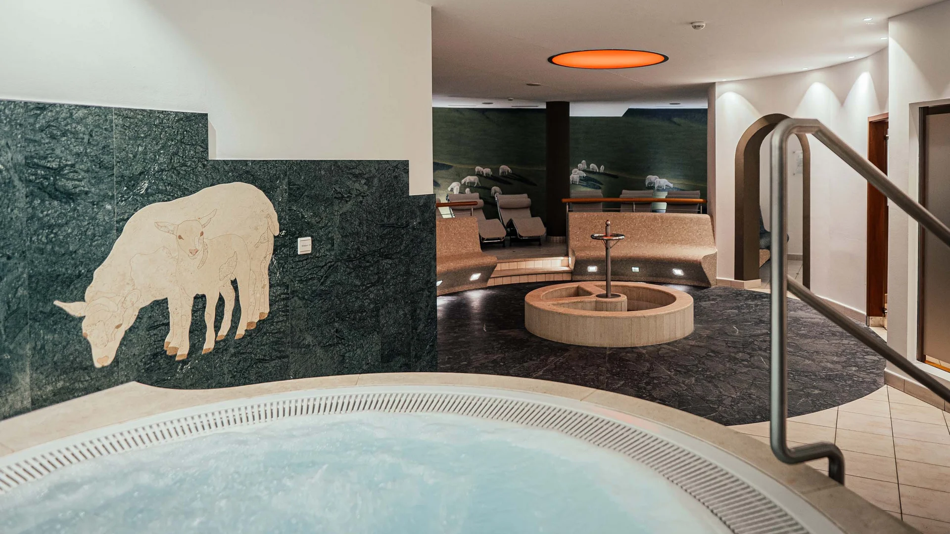 Indoor spa area with a hot tub, seating area, and a sheep mosaic on the wall