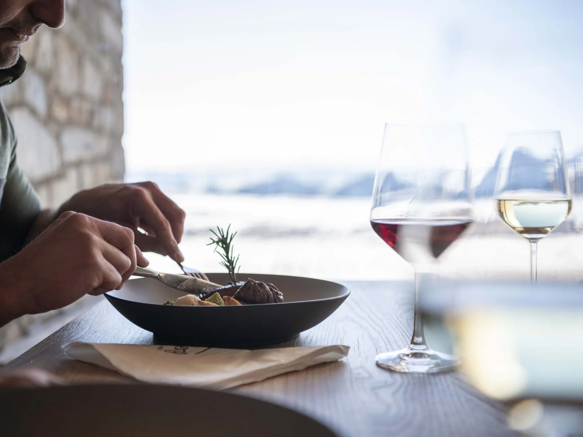 Il Lodenwirt a Vandoies | Hotel, residence e ristorante Un ospite gusta un piatto con due calici di vino vicino a una finestra