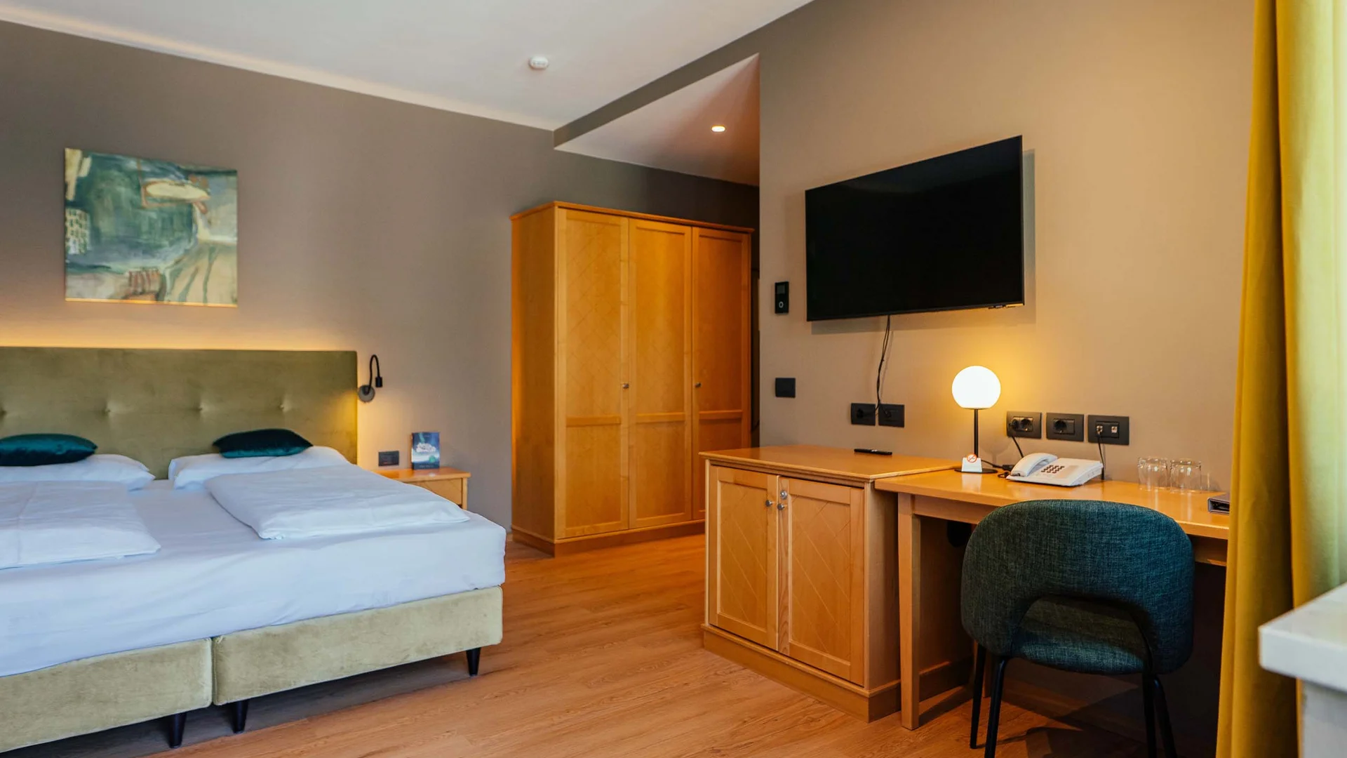 Hotelzimmer mit Doppelbett, Schrank, Schreibtisch, Stuhl und Wandfernseher