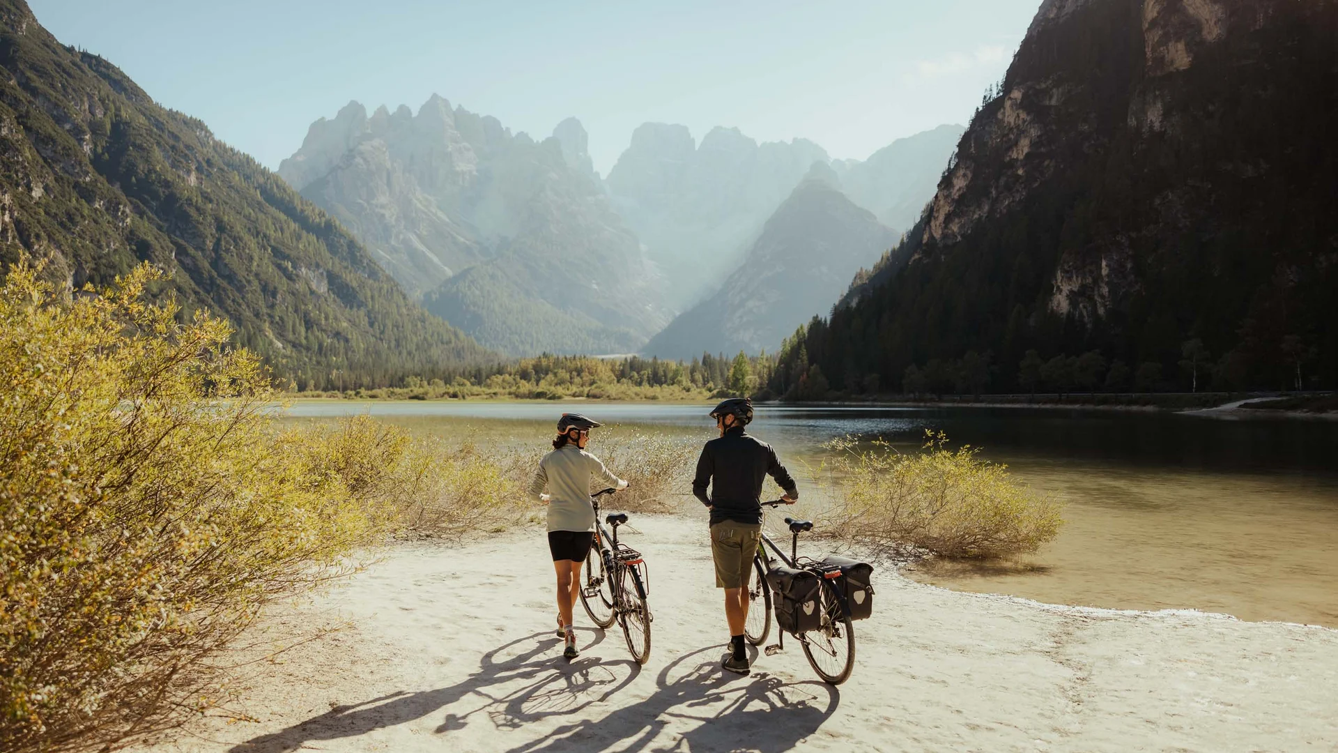 Due ciclisti camminano con le loro biciclette vicino a un lago di montagna