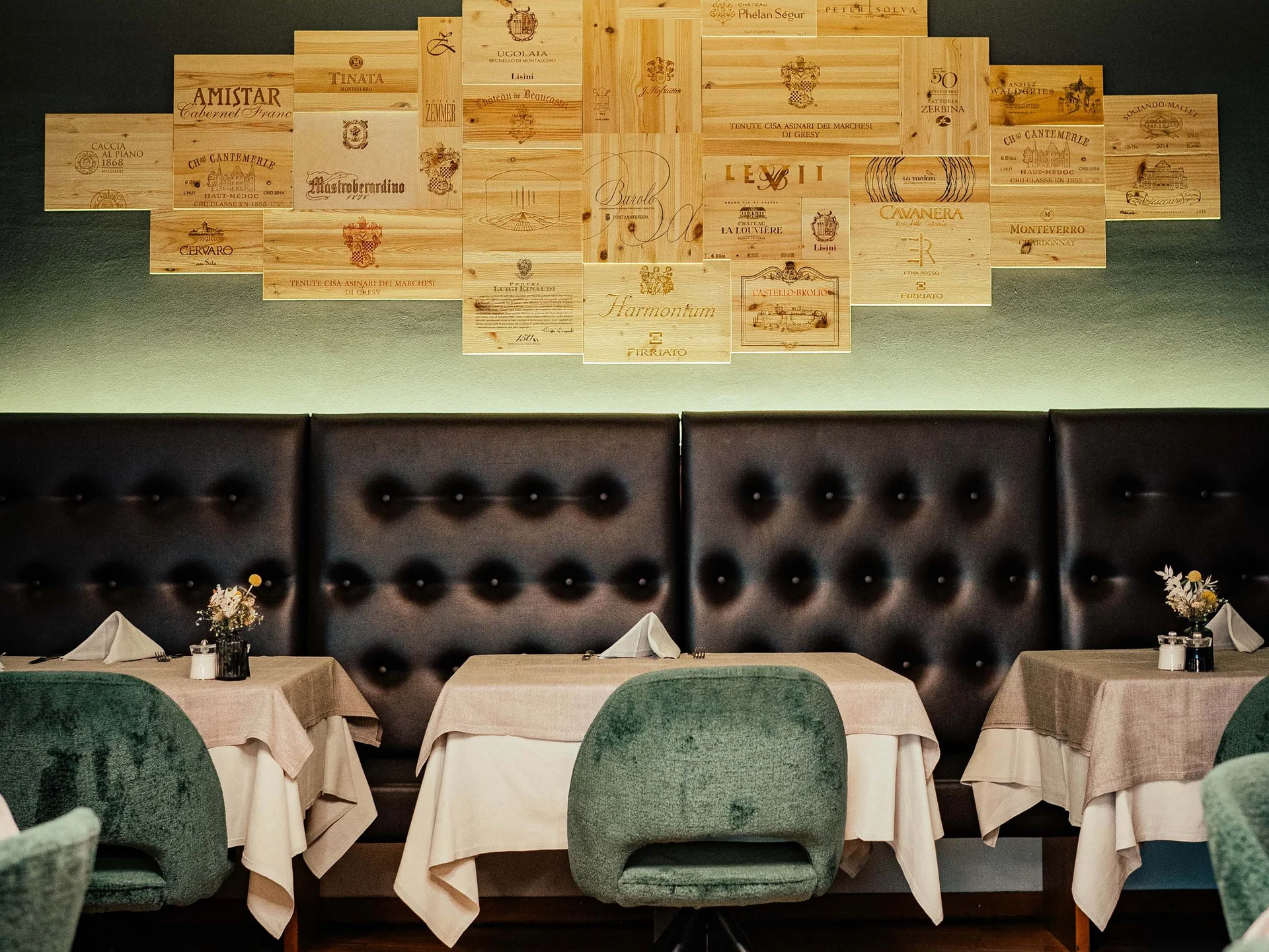 Area ristorante accogliente con sedie verdi e decorazioni murali di casse di vino