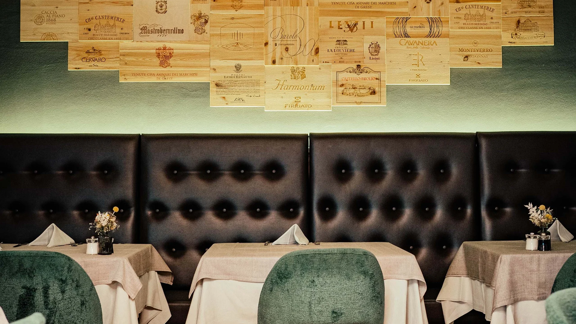 Area ristorante accogliente con sedie verdi e decorazioni murali di casse di vino