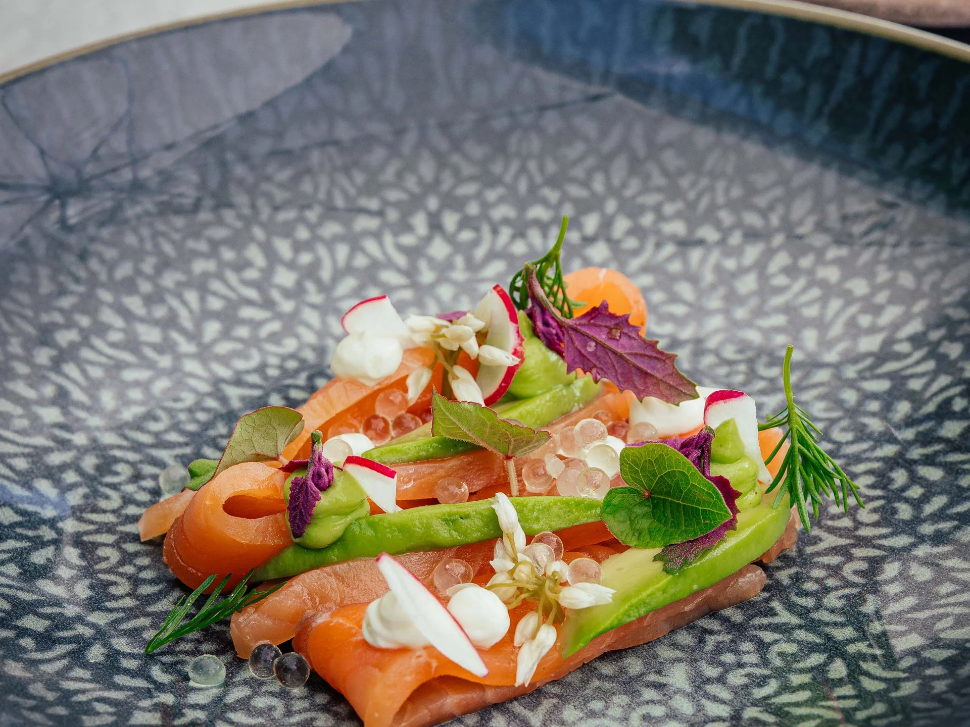 Salmone finemente decorata con erbe e fiori commestibili su piatto blu