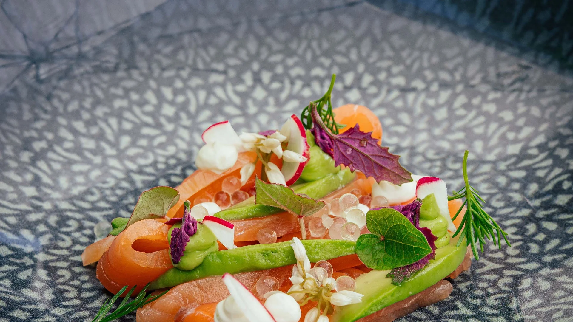 Salmone finemente decorata con erbe e fiori commestibili su piatto blu