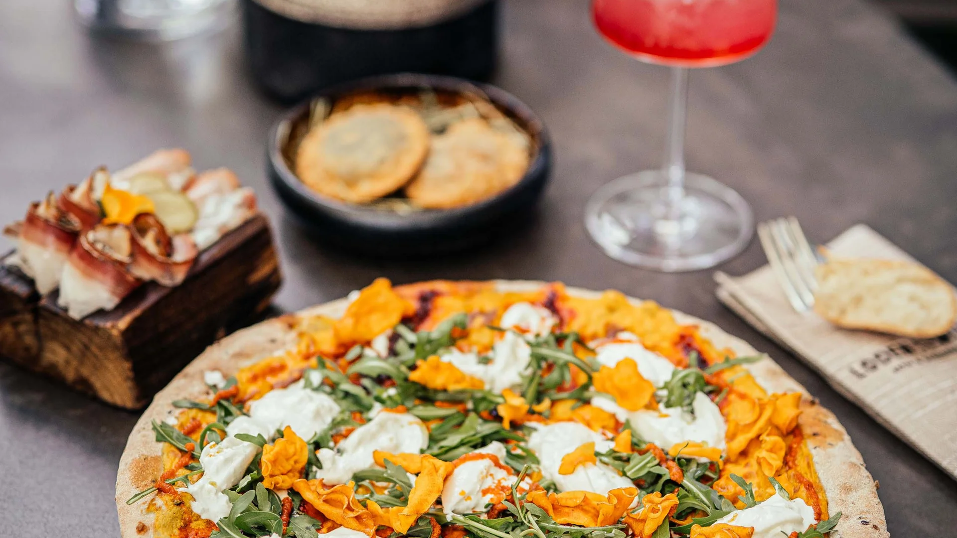 Pizza con rucola, formaggio e fiori di zucca su tavolo con bevande e snack