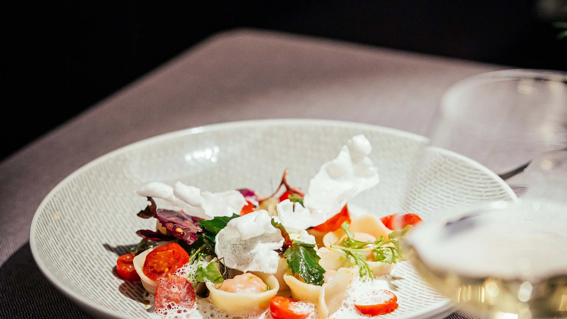 Fein angerichtete Pasta mit Tomaten, Blättern und Schaum auf weißem Teller