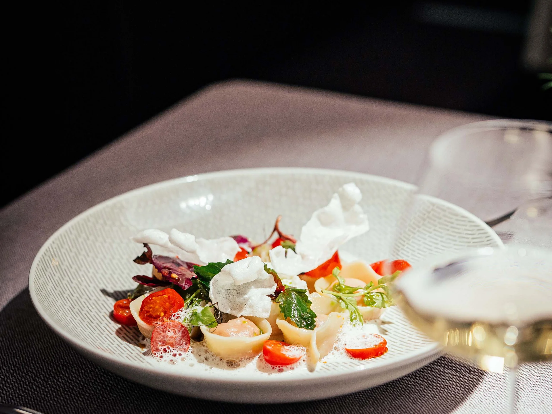 Fein angerichtete Pasta mit Tomaten, Blättern und Schaum auf weißem Teller