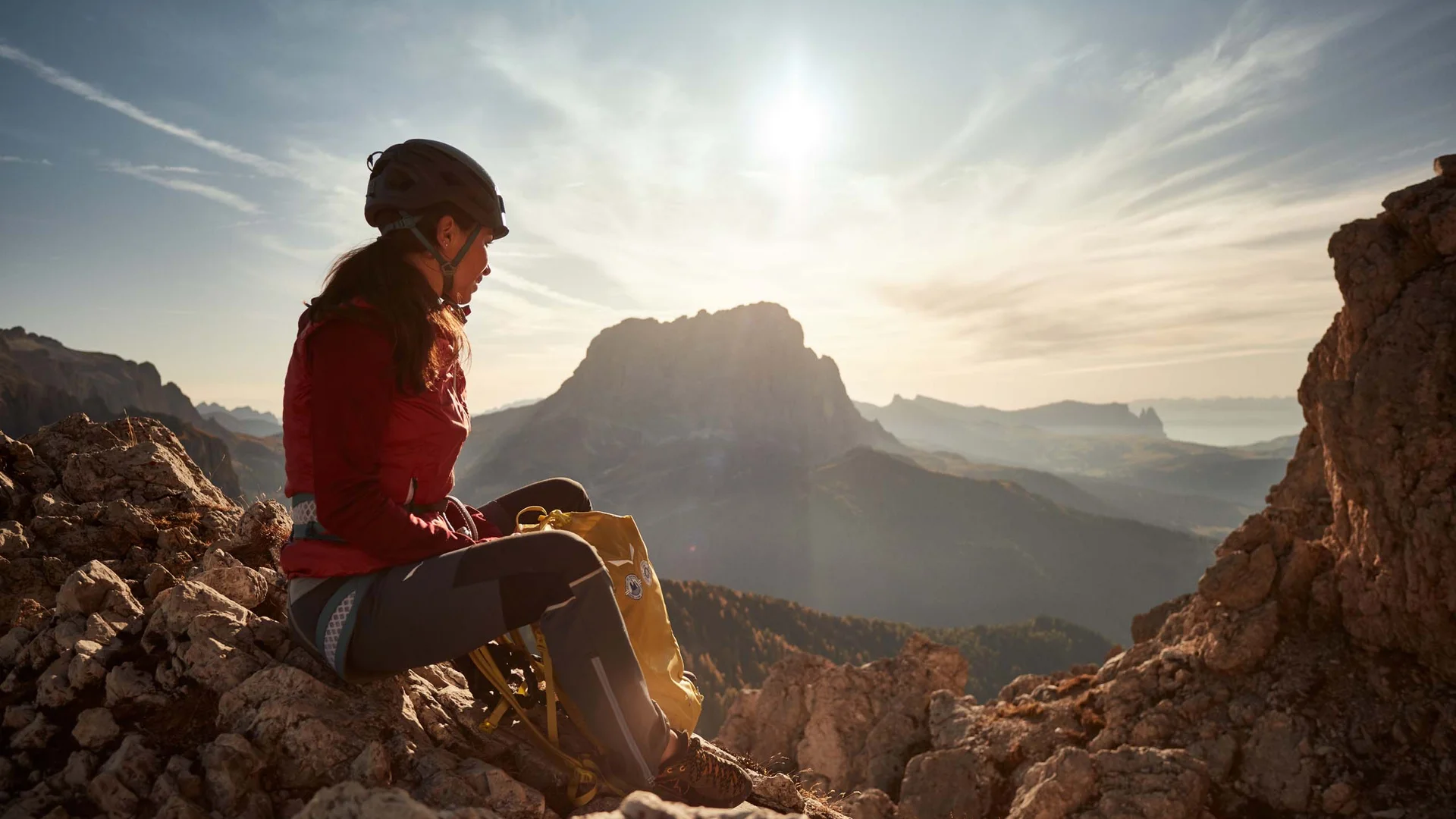 Alpinista con casco su una vetta rocciosa all’alba