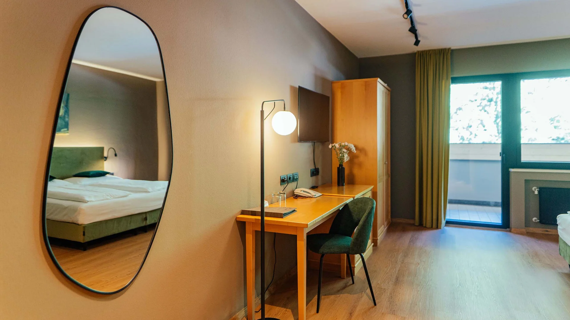 Hotelzimmer mit Schreibtisch, Stuhl, großem Spiegel und Balkon