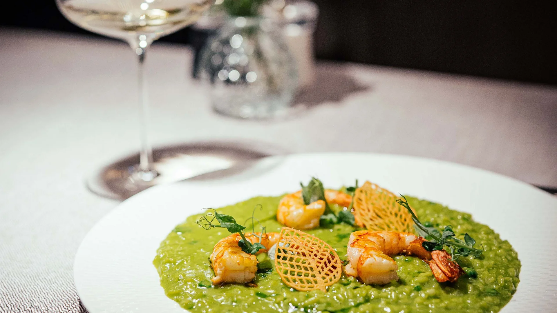 Risotto verde con gamberi e chips croccanti su piatto bianco