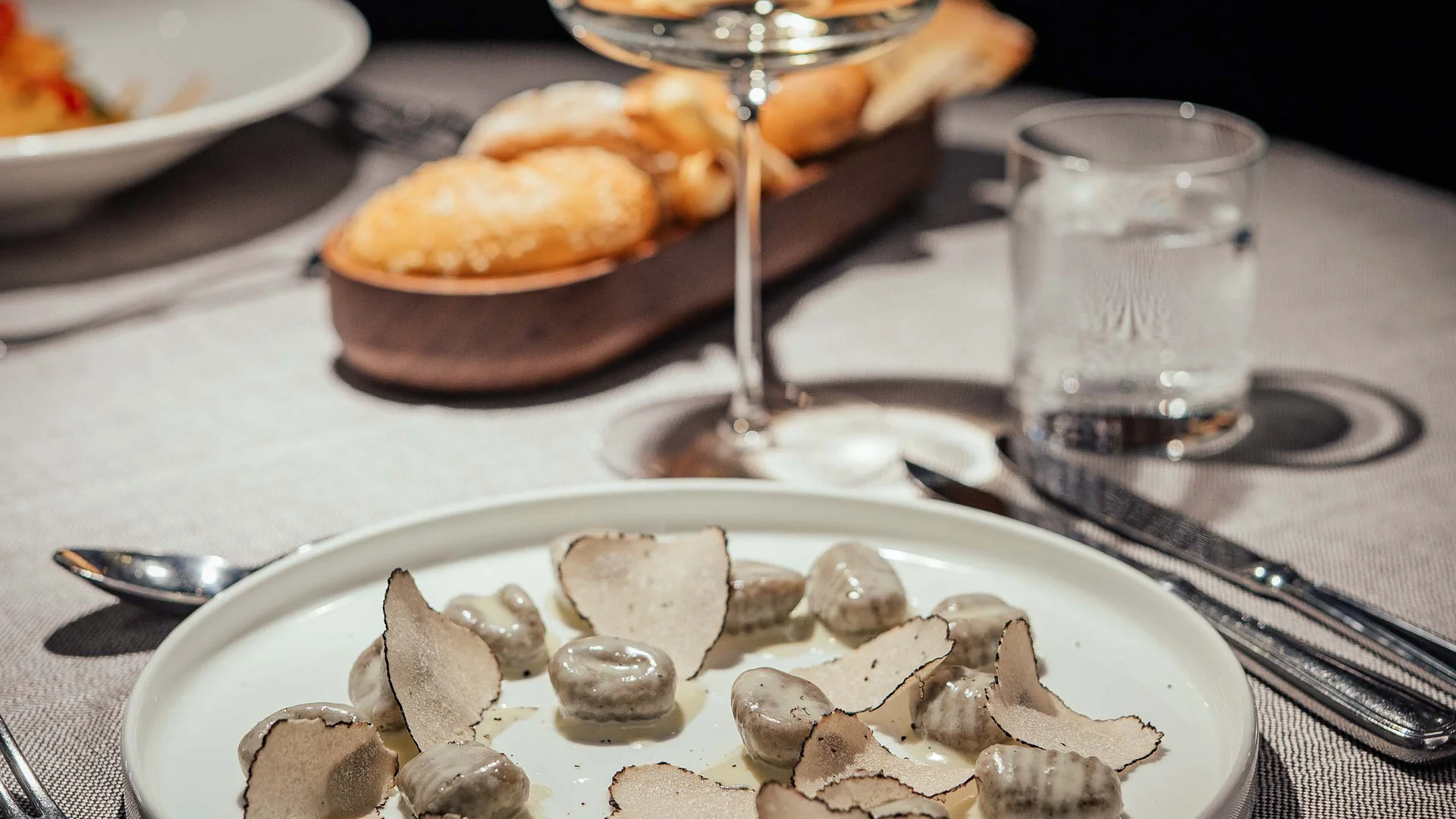 Gnocchi con scaglie di tartufo su piatto bianco con vino e pane sullo sfondo