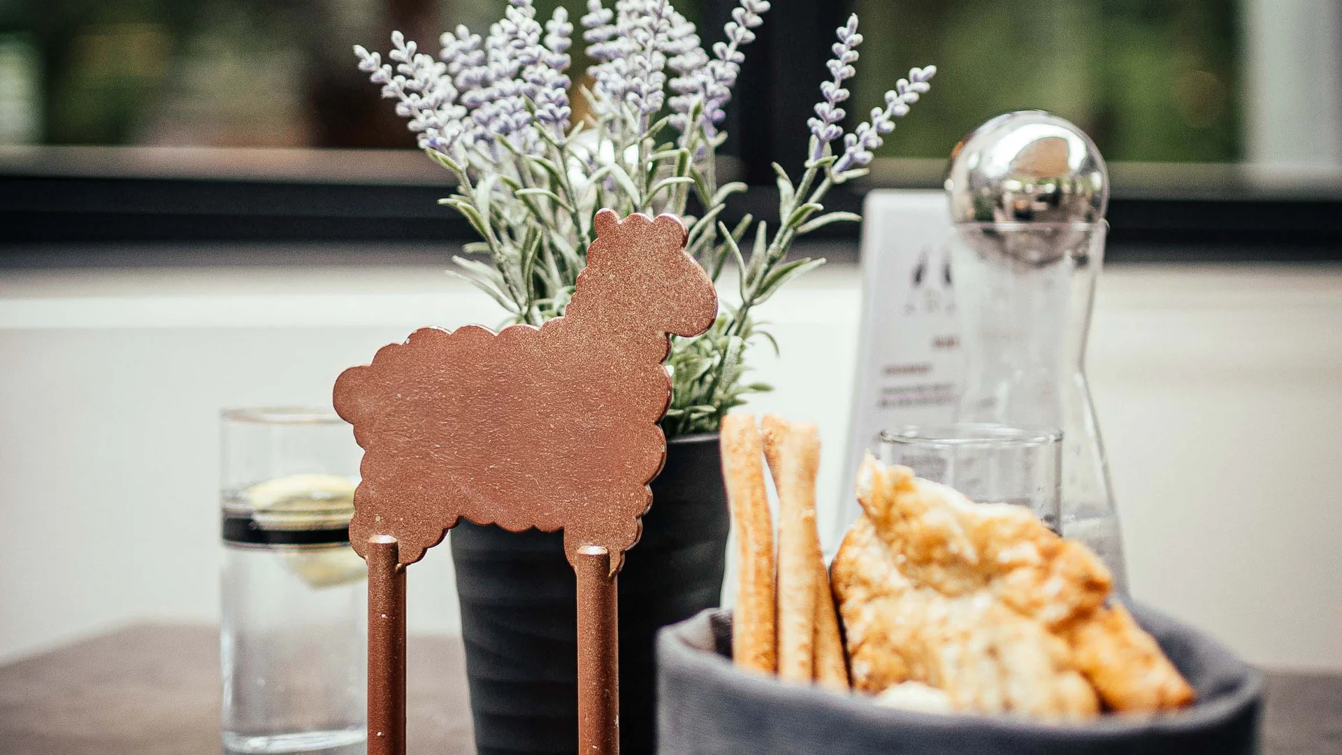 Tavolo con pane, bicchiere d'acqua, pianta di lavanda e segnaposto a forma di pecora