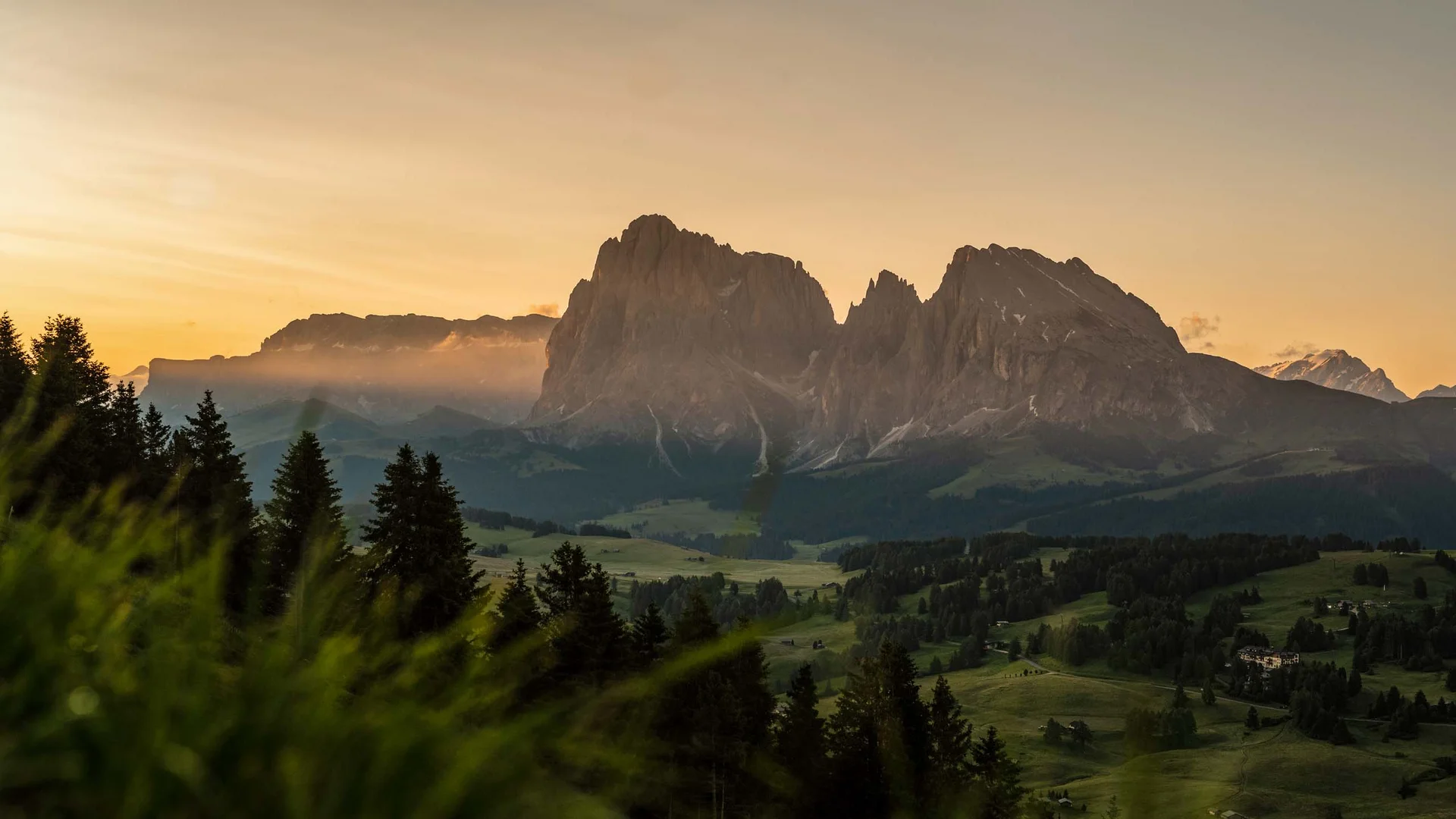 Paesaggio montano al tramonto con pendii boscosi e prati verdi