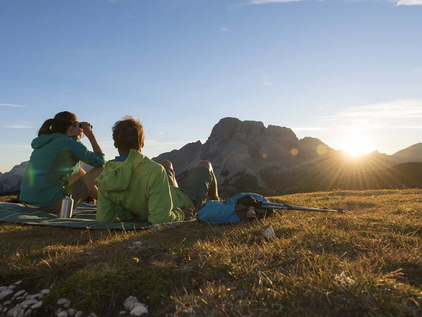 Le vostre vacanze in Val Pusteria Due escursionisti seduti su un prato guardano le montagne al tramonto