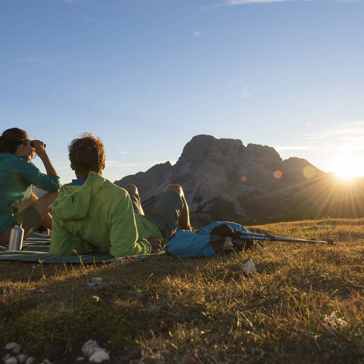 Le vostre vacanze in Val Pusteria Due escursionisti seduti su un prato guardano le montagne al tramonto