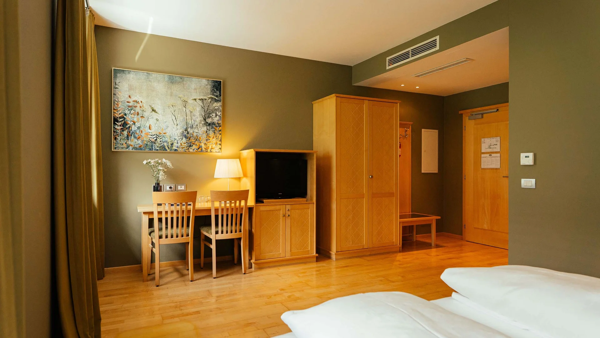 Camera d'hotel con mobili in legno, TV, tavolo, sedie e letto matrimoniale