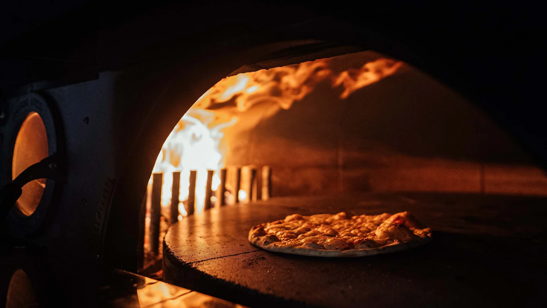 Pizza che cuoce in un forno a legna con fiamma aperta