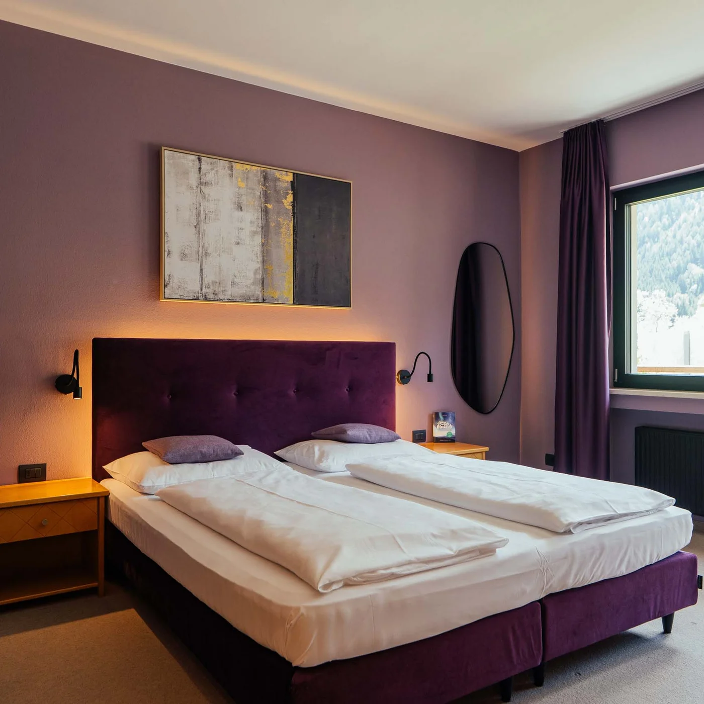 Seminarhotel in Südtirol | Tagen im Lodenwirt Modernes Hotelzimmer mit Doppelbett, lila Kopfteil und Blick auf Berge