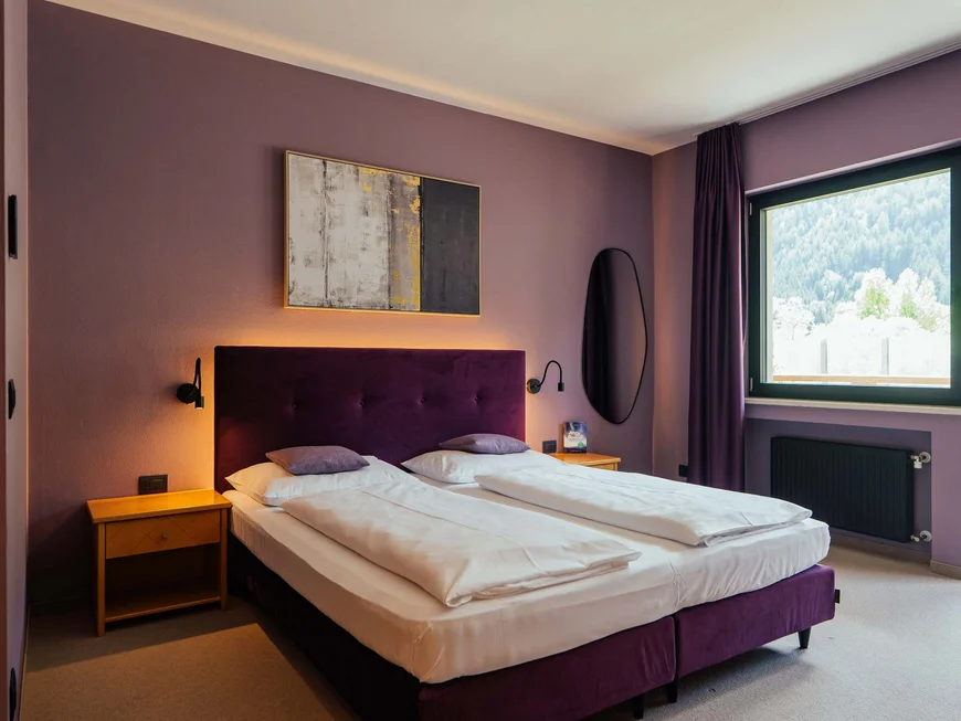 Seminarhotel in Südtirol | Tagen im Lodenwirt Modernes Hotelzimmer mit Doppelbett, lila Kopfteil und Blick auf Berge