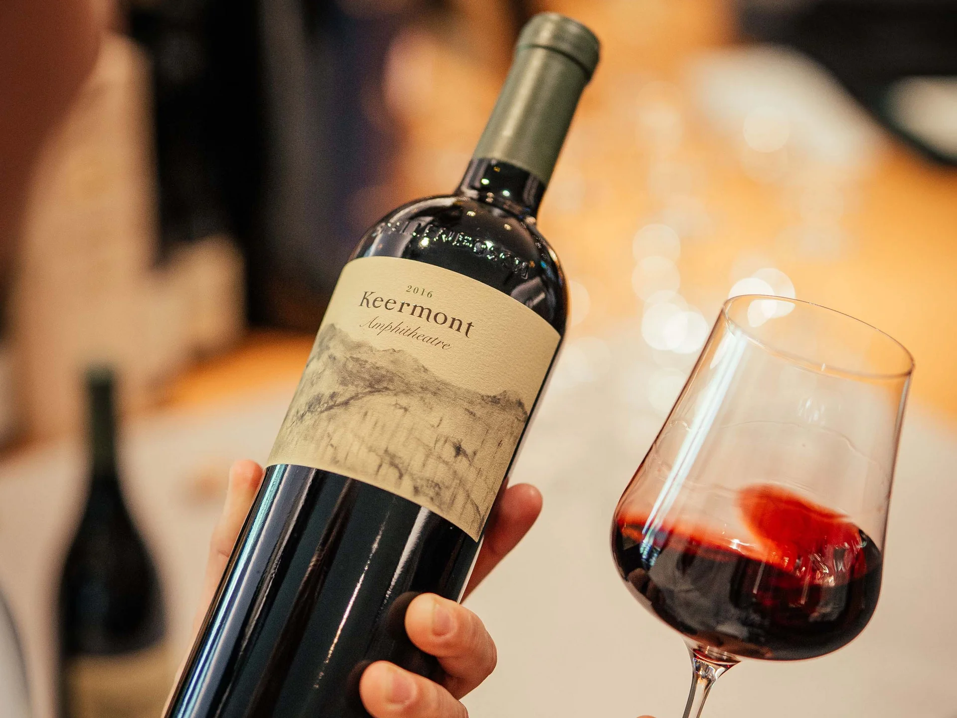 Persona che tiene una bottiglia di vino e un bicchiere di vino rosso