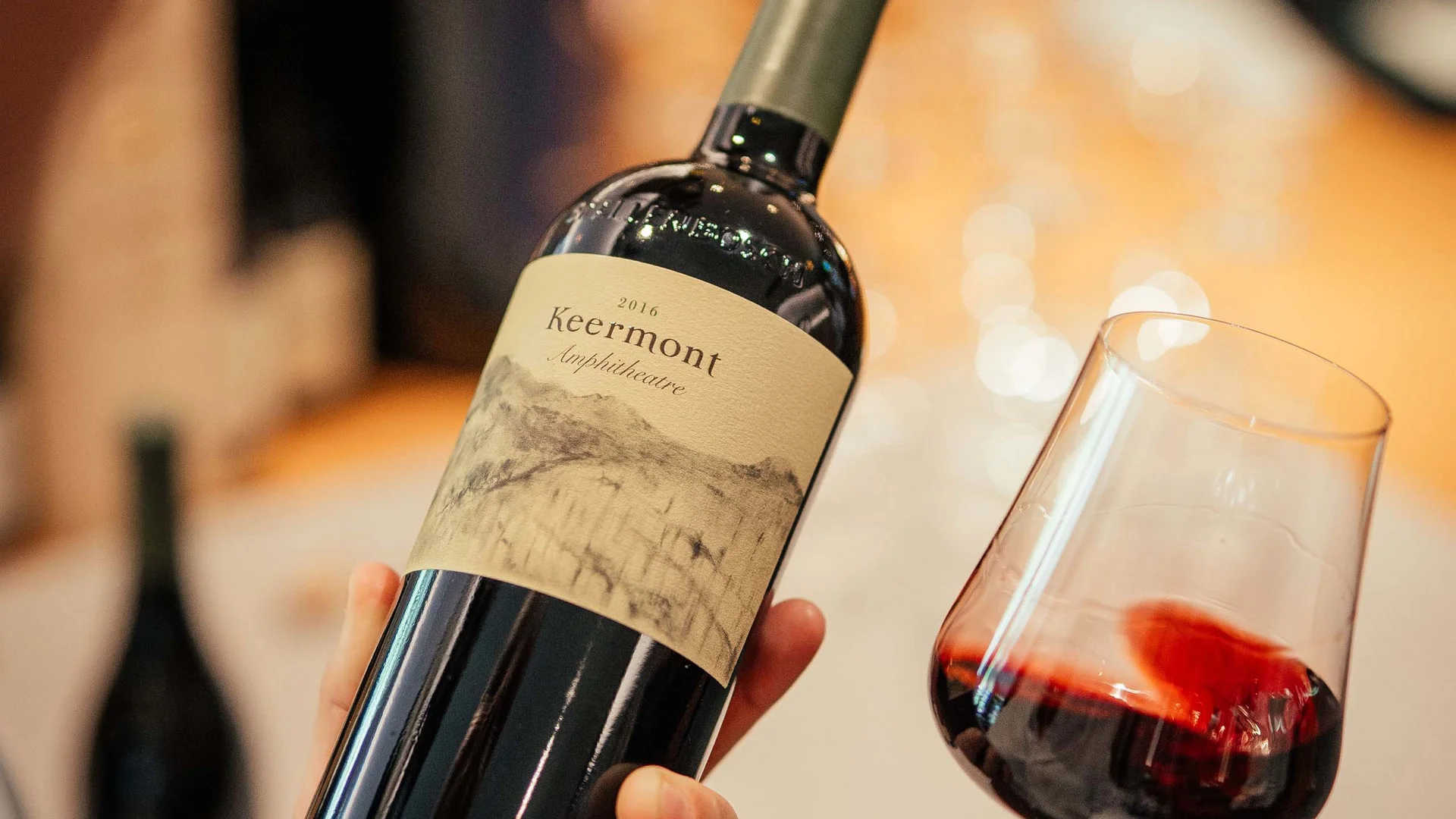 Persona che tiene una bottiglia di vino e un bicchiere di vino rosso