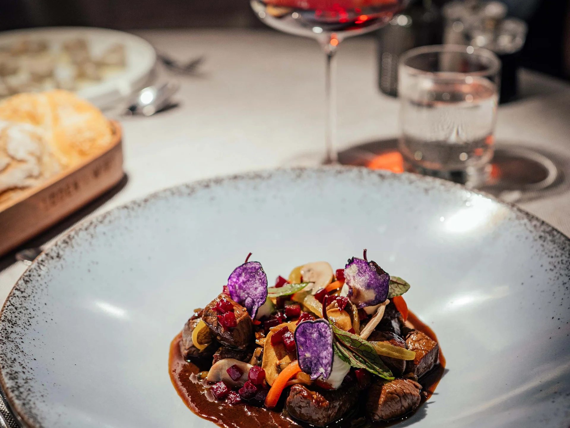 Piatto gourmet con carne, verdure e chips viola su piatto bianco