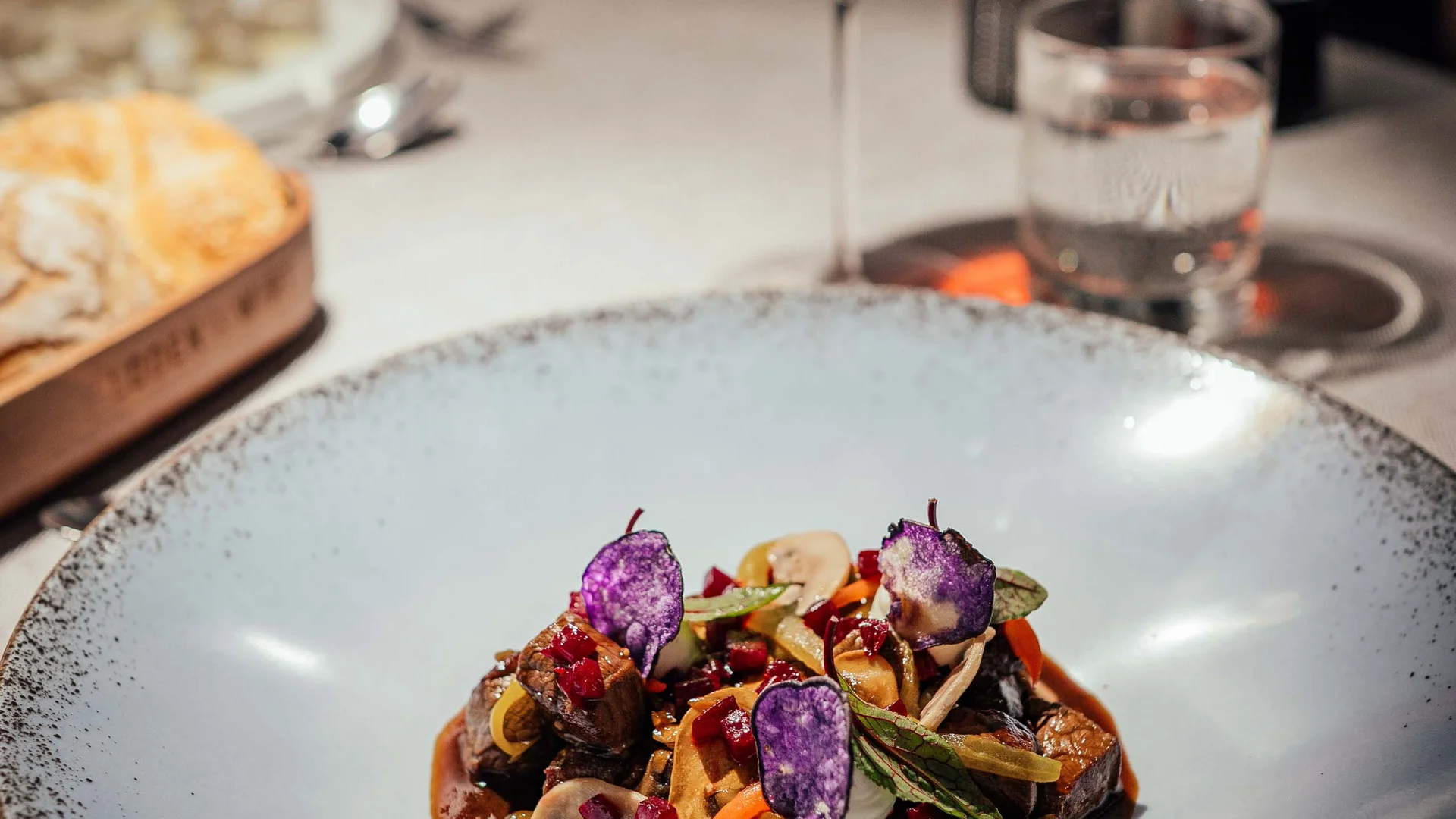 Piatto gourmet con carne, verdure e chips viola su piatto bianco