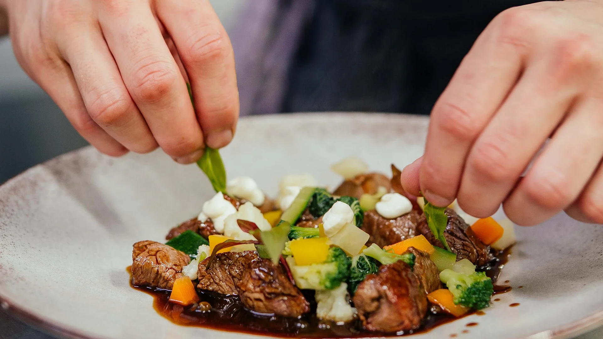 Cuoco decora piatto con pezzi di carne e verdure colorate