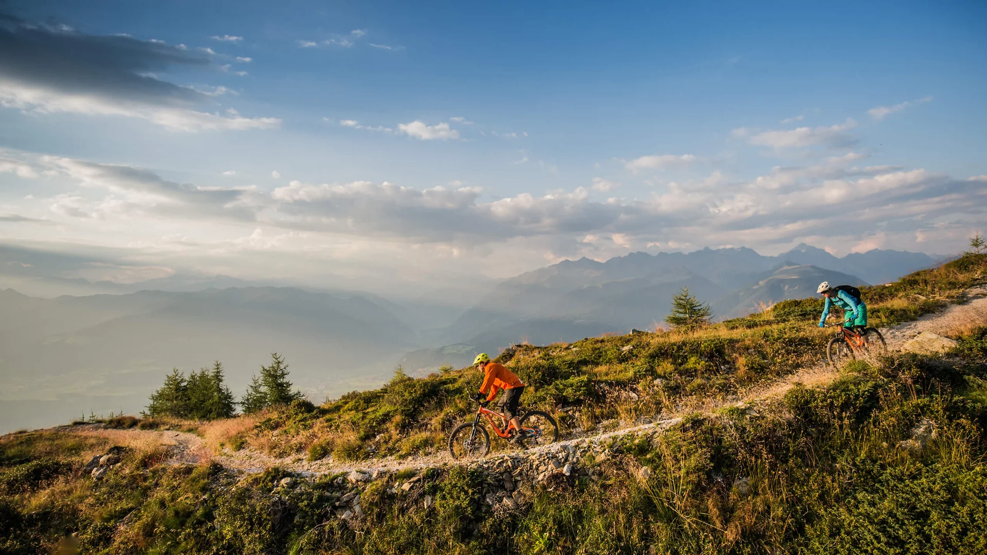 Due ciclisti di mountain bike percorrono un sentiero alpino con montagne sullo sfondo
