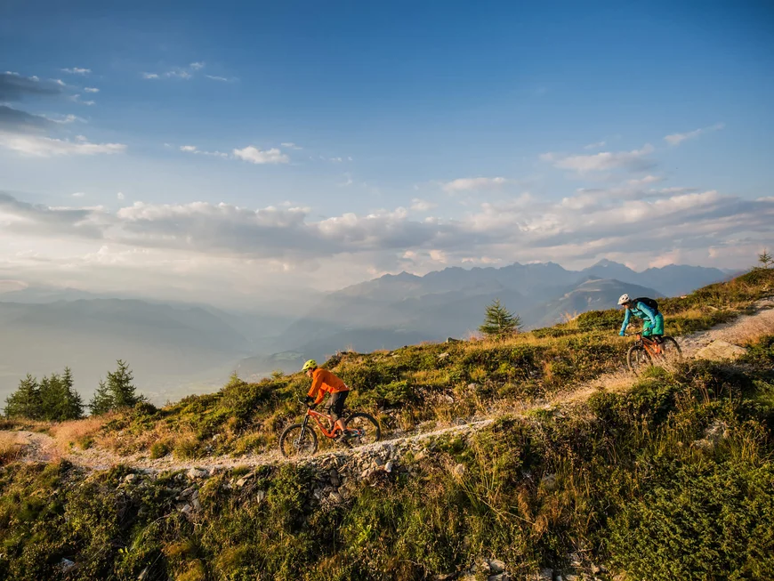 Le vostre vacanze in Val Pusteria Due ciclisti di mountain bike percorrono un sentiero alpino con montagne sullo sfondo