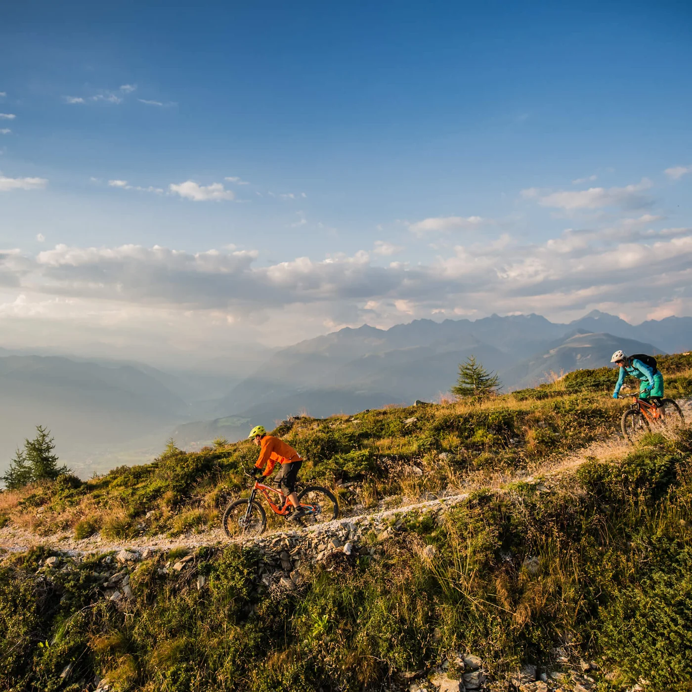 Le vostre vacanze in Val Pusteria Due ciclisti di mountain bike percorrono un sentiero alpino con montagne sullo sfondo