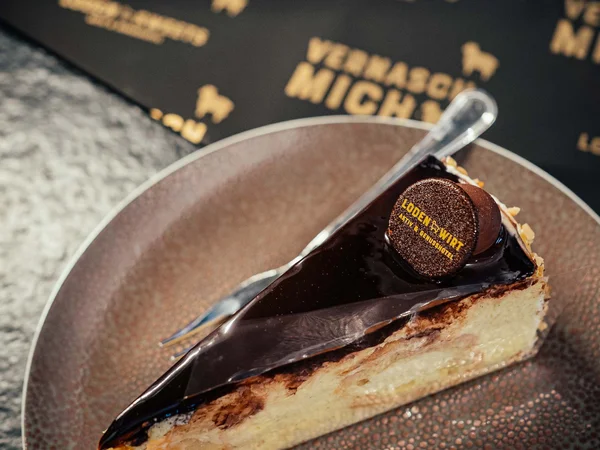 Stück Kuchen mit Schokoladenglasur und Dekoration auf braunem Teller