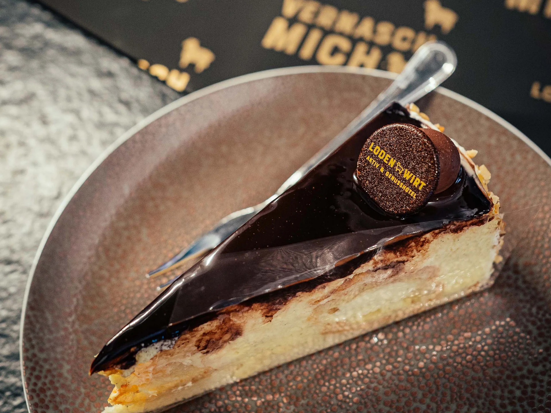 Der Lodenwirt in Vintl | Hotel, Residence & Restaurant Stück Kuchen mit Schokoladenglasur und Dekoration auf braunem Teller