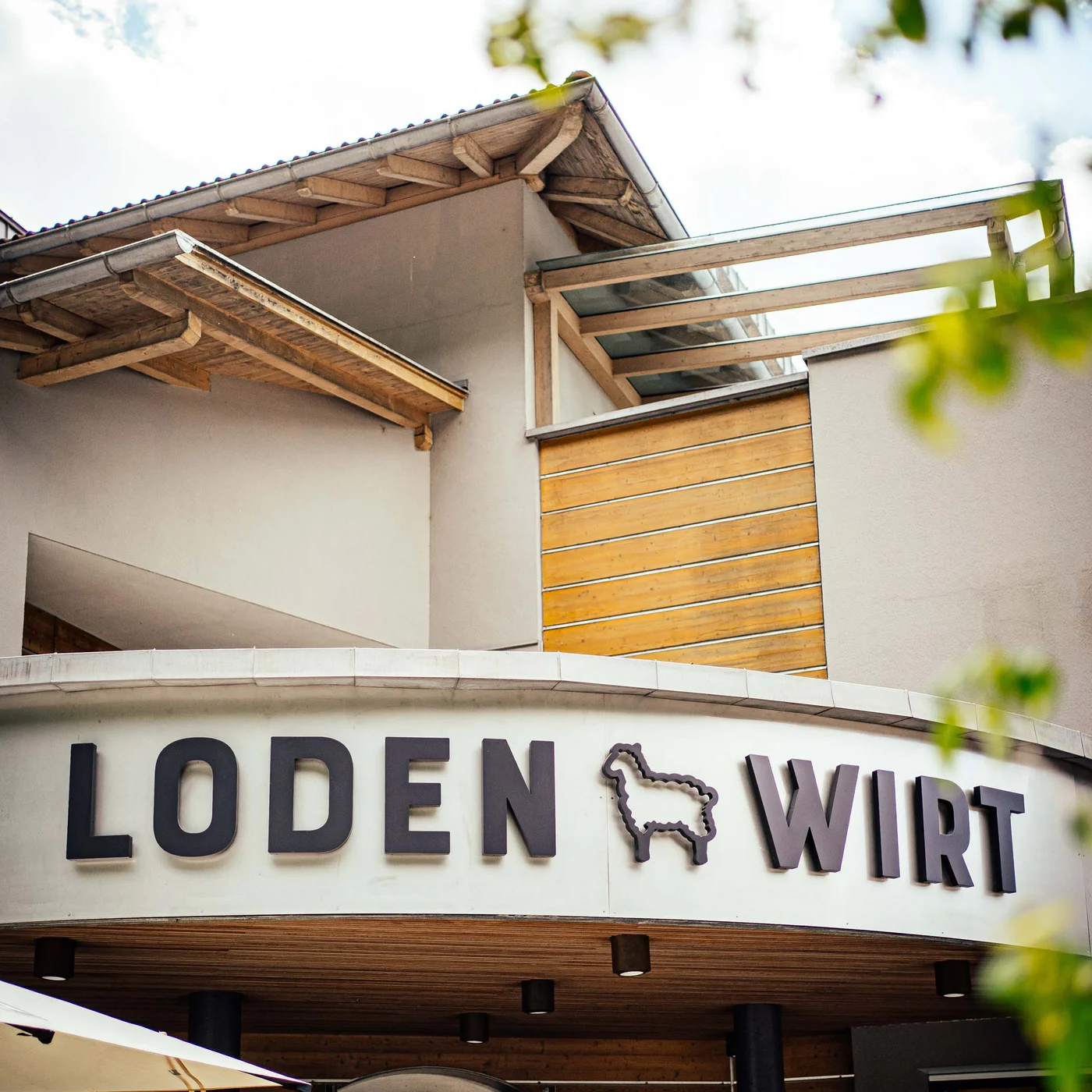 Der Lodenwirt in Vintl | Hotel, Residence & Restaurant Eingang eines Gebäudes mit Schriftzug Loden Wirt und Schaf-Logo